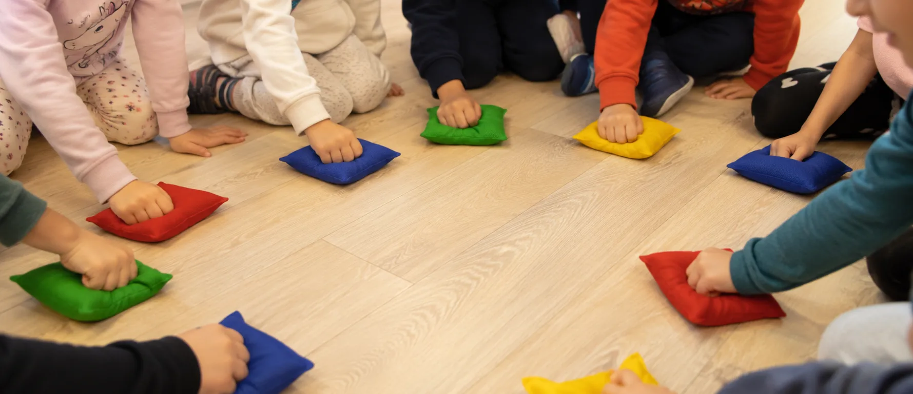 Un grupo de niñas y niños sentados en corro en el suelo, cada uno con la mano apoyada sobre un saquito de color